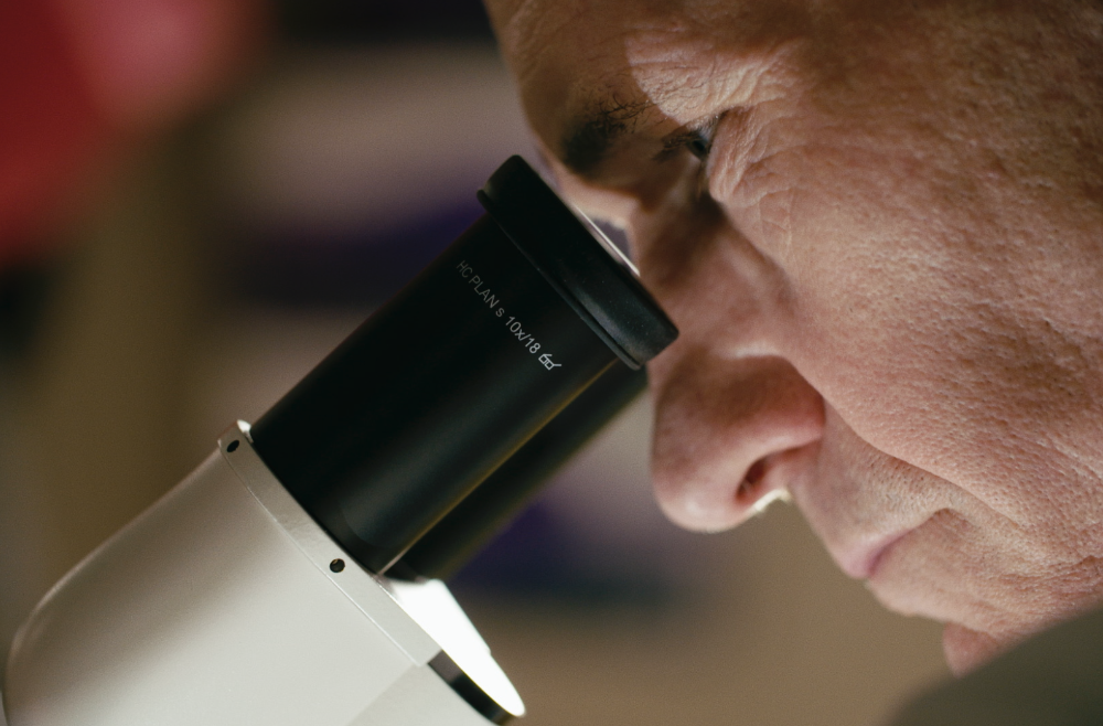 A close up photo of Carl June looking into a microscope.
